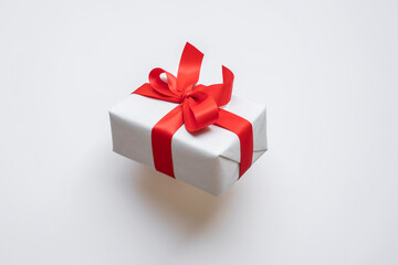 Obraz premium Simple white paper craft gift box with red ribbon bow in dynamic angle.anniversary and special day with present