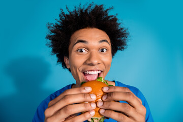 Photo portrait of attractive young man eat burger bite dressed stylish clothes isolated on blue...