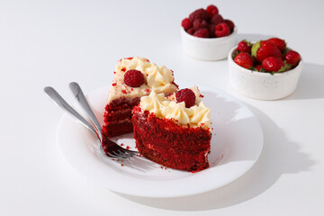 Pieces of red velvet cake on plate and berries on white background