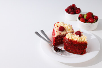 Pieces of red velvet cake on plate and berries on white background, space for text