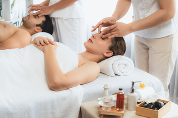 Caucasian couple enjoying relaxing anti-stress head massage and pampering facial beauty skin recreation leisure in dayspa modern light ambient at luxury resort or hotel spa salon. Quiescent