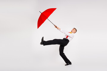 Young man in elegant attire with vibrant red umbrella showcasing energetic dance move on white...