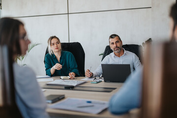 A diverse group of business people engaged in a meeting around a table, discussing project details...