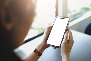 Person with metallic watch holding smartphone showing blank screen by window, demonstrating minimalist mockup for digital interface design.