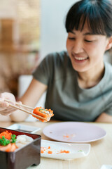 Asian woman enjoying sushi with chopsticks at restaurant