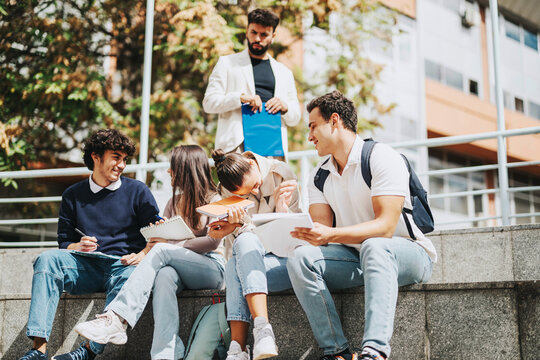 A group of high school students sits outdoors, discussing and solving tasks with a teacher offering guidance. The setting is lively, promoting teamwork and learning amidst nature.