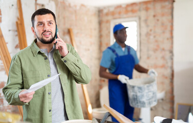 Portrait of irritated young man architect emotionally talking on phone at indoor building construction site, having problems with contractor