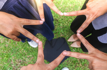Hands joined together forming a star with v-sign with a graduation cap in the background. Graduation friendship and teamwork concept.