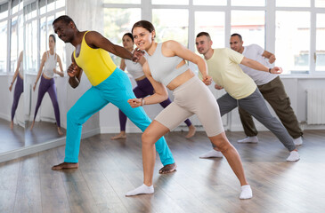 Obraz premium European girl teaches sequences of movements, actions during dance lesson, trains to doing elements of electro dance, enjoys active hobby. Multinational group rehearsal, dance choreography coach