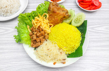 Yellow rice with side dishes of chicken, tempeh, scrambled eggs, noodles and chili sauce is served on a plate. Indonesian style yellow rice