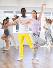 Fototapeta premium Slim middle-aged man and woman practicing salsa dance in training hall during group dancing classes