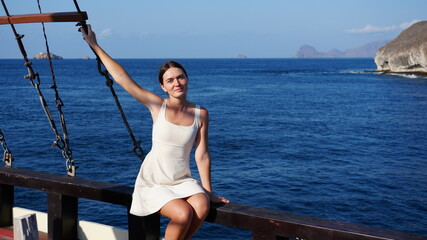Young beautiful slim woman in white dress traveling on yacht. Beautiful woman posing for photo on yacht during vacation in Indonesia
