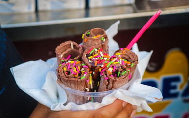 Chocolate Stir-fried ice cream Roll with meses topping in a cup made by hand. Hand holding a bowl of rolled ice cream