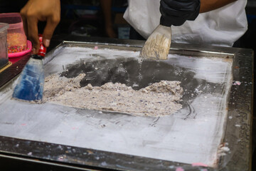 Roll a vanilla ice cream to prepare a cup of chocolate-wrapped ice cream. Man rolls ice cream, spatula scrapes strawberry ice cream into rolls on frozen machine