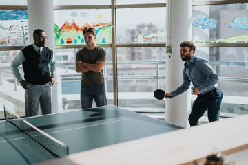 Multicultural business workers take a break to play ping pong in a bright, modern office. The scene...