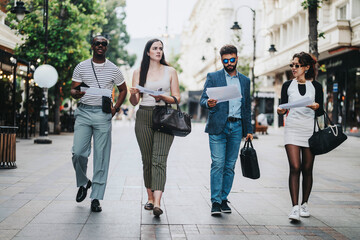 A diverse group of professionals walking on a city street, engaged in a business discussion. They are holding documents and bags, reflecting teamwork and urban lifestyle.