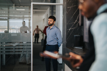 A diverse group of business people engage in a discussion in a modern office hallway, showcasing teamwork and communication dynamics.