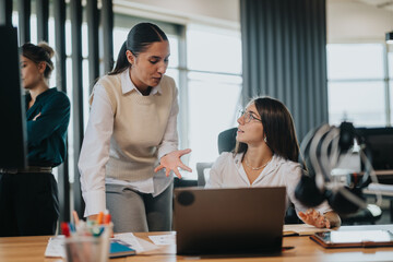 Two business people engaged in a conversation at a desk, demonstrating teamwork and communication in a contemporary workplace environment.