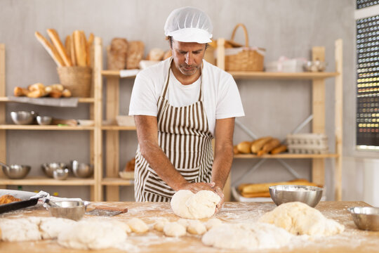 Adult man baker kneading dough for baking on table