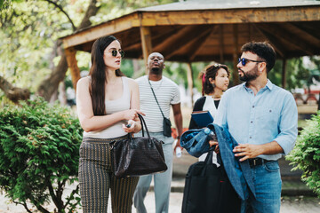 A group of diverse business people engage in a casual conversation outdoors. The setting is a park, providing a relaxed atmosphere, with trees and greenery in the background.