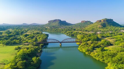 Scenic Aerial View of River and Bridge Surrounded by Lush Green Hills and Clear Sky