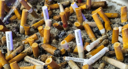 Cigarette butts in an ashtray labeled with different side effect diseases that smoking can cause