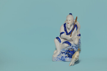 Porcelain figurine of a traditional Chinese fisherman holding a fishing rope with a fish isolated...