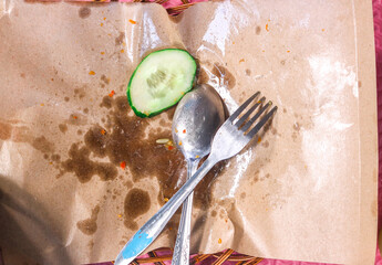 Leftover food wrapped in paper with spoon and fork.