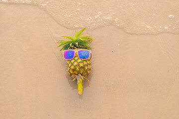 Pineapple wearing sunglasses lying on the sand.