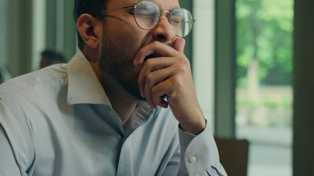 Tired exhausted bored business man Indian Arabian guy male businessman freelancer student teacher study write notes notebook yawning sleepy weary lack sleep drink morning coffee in cafe surging energy