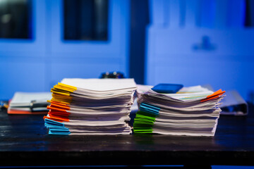 A quiet office desk at night, illuminated by a desk lamp. Documents, papers, and files are...