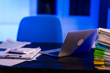 A quiet office desk at night, illuminated by a desk lamp. Documents, papers, and files are...