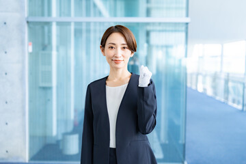 室内で手袋をつけてガッツポーズをしてカメラ目線のスーツを着た女性