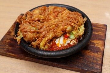 Crispy omelet complete with spicy chili sauce on a black plate in close view on the table.