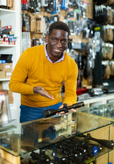 Fototapeta premium African-american man seller standing at counter in arms shop and presenting rifle telescope.