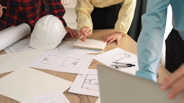 Architect and safety engineer discussion about building blueprint displaying on laptop on table with architectural document and wooden block scatter around at modern office. Closeup. Delineation.