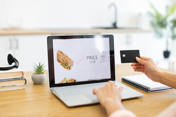 Caucasian woman shops online using laptop, choosing food from delivery site. She makes payment with...