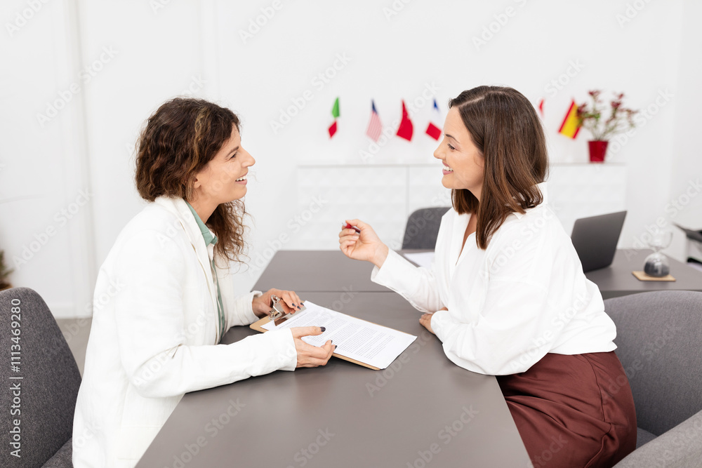 Poster two caucasian women are having a productive conversation at a sleek office desk. they are sharing id