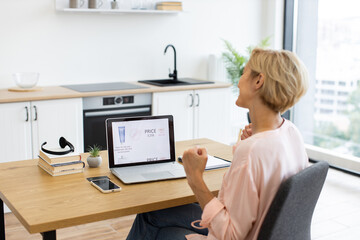 Happy Caucasian woman celebrating success while ordering cosmetics online using laptop. She sits in...