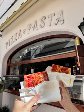 Hand grabbing a slice of italian pizza with cheese and tomato sauce at italian pizzeria Capri, Italy.