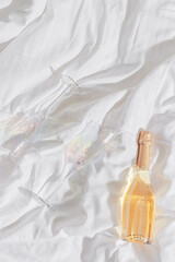 Romance concept, lifestyle photo minimal style, two bright glasses with rainbow shadow, white wine bottle on white bedclothes at home, natural light, top view close up, star filter, copyspace