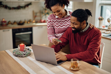 Happy black couple using credit card while making online reservation for Christmas.