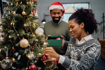 Happy black woman decorating Christmas tree with her husband at home.