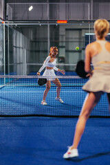 Two girls playing padel on a blue indoor court