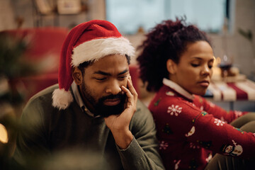 Displeased African American couple sitting at home on Christmas Eve.