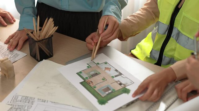 Smart architect and safety engineer discussion about building blueprint on table with architectural document, measurement tools and wooden block scatter around at modern office. Closeup. Delineation.