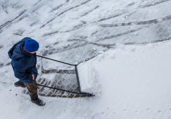 A man in a blue jacket is shoveling snow with a snow plow
