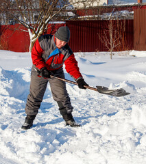 A man in a red jacket and gray pants is shoveling snow
