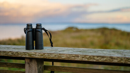 Black Binoculars on a Wooden Railing Overlooking the Coastline at Sunset for Birds, Wildlife and Seascape Viewing
