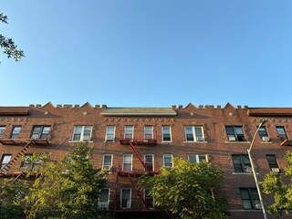Red brick apartment building, fire escapes, trees against blue sky
